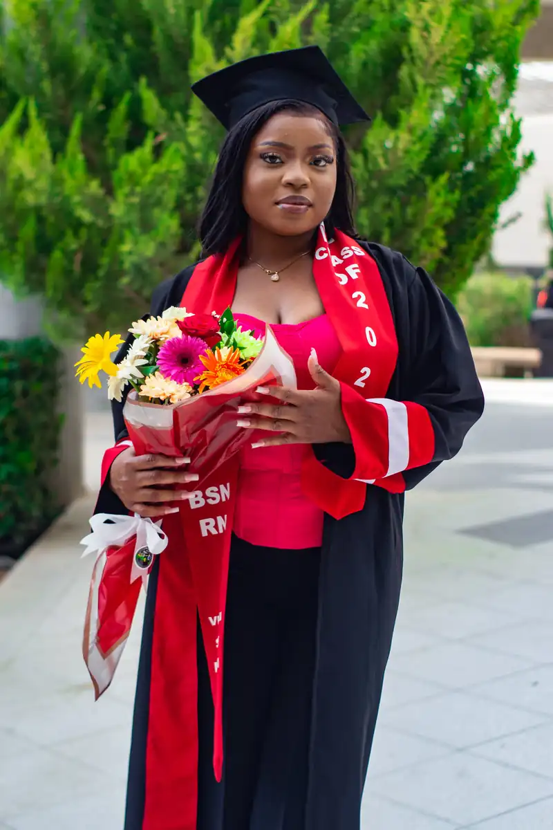 Graduate holding a bouquet while wearing a black gown with red accents