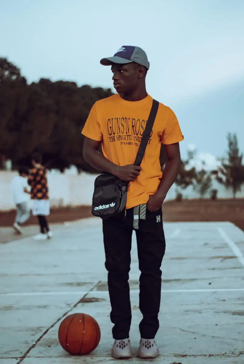 Young man in an orange shirt standing beside a basketball outdoors