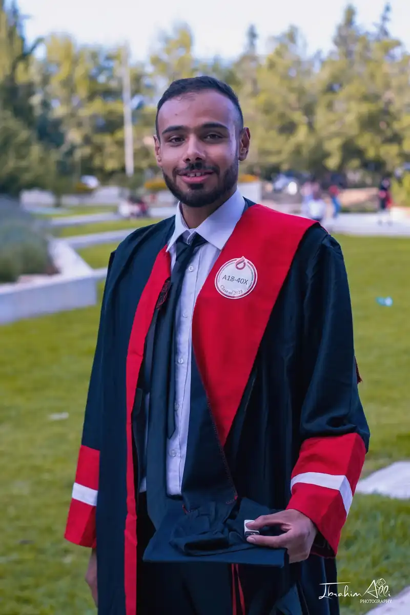 Graduate wearing a black gown and red stole outdoors