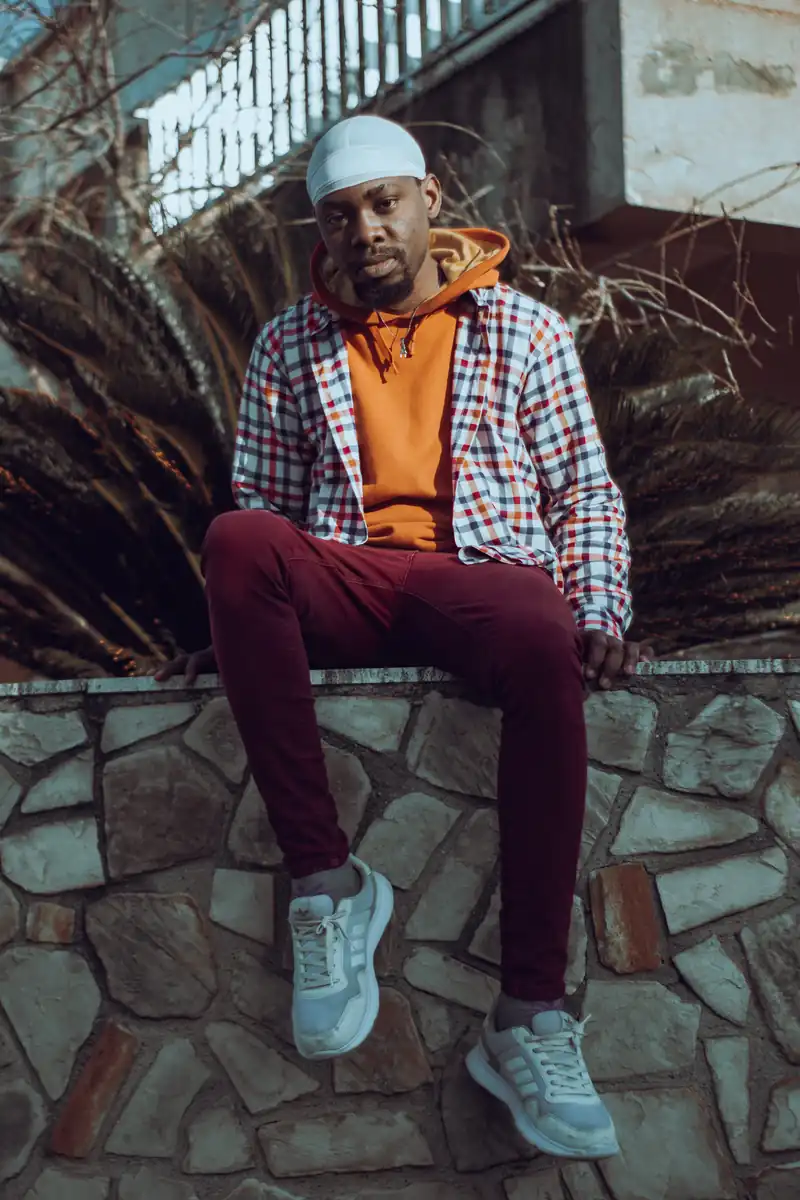 Seated outdoor portrait in an orange hoodie and checked overshirt